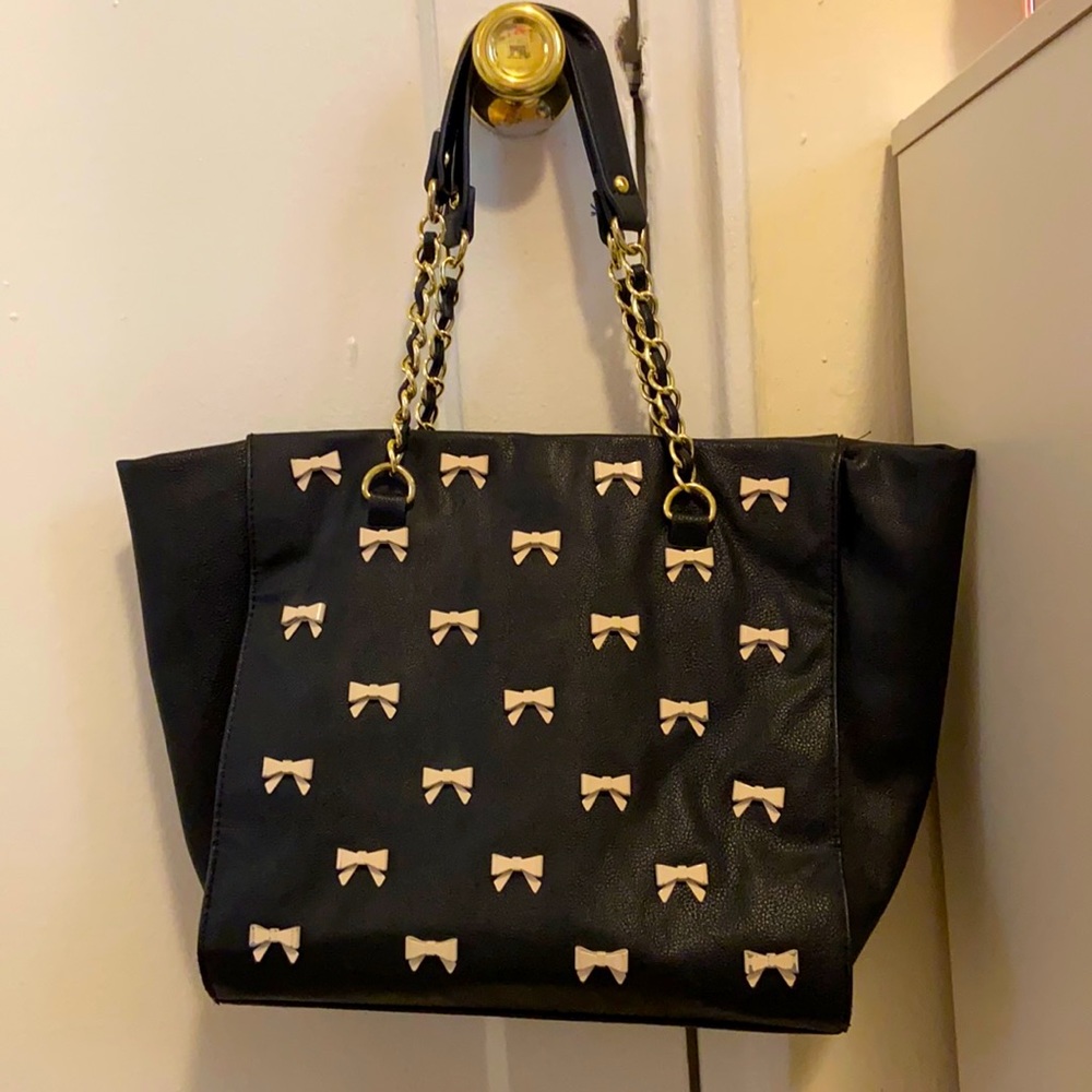 A black purse with pink bows in front.